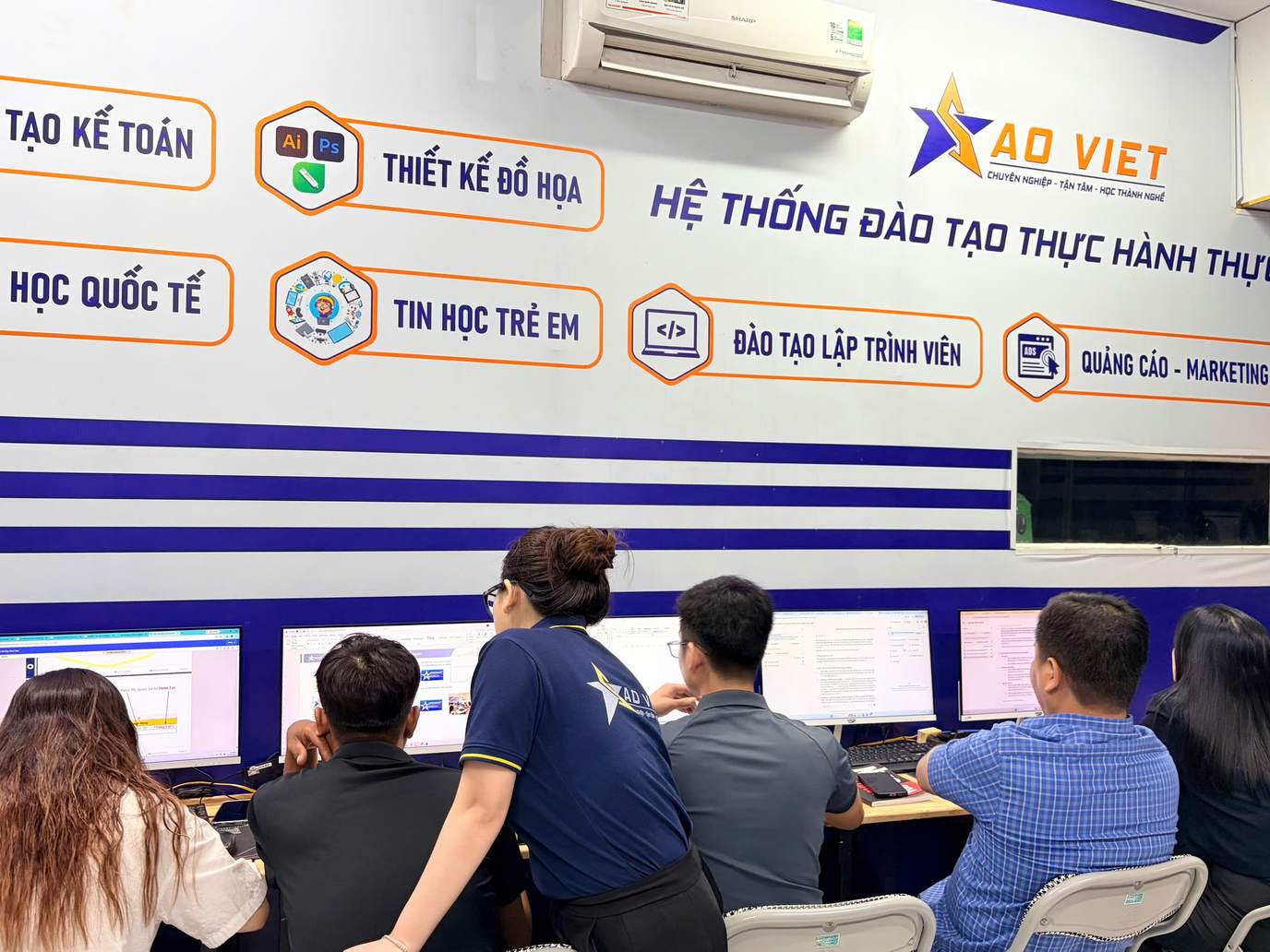 Giảng viên hướng dẫn nhóm học viên tại lớp học máy tính